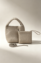 A woven leather handbag and matching small pouch with a wrist strap, displayed on a warm beige studio background. The handbag has a top handle, a long chain strap, and a zip-top closure.