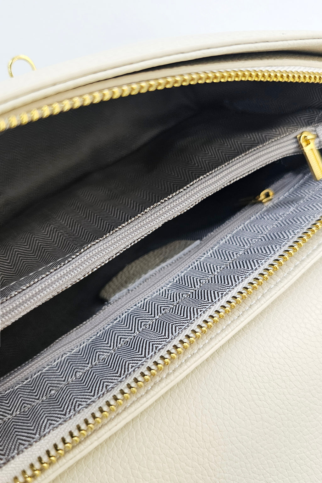 Close-up of a cream-colored handbag showing its interior compartments with gold-tone zippers and a gray patterned lining.