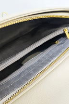 Close-up of a cream-colored handbag showing its interior compartments with gold-tone zippers and a gray patterned lining.