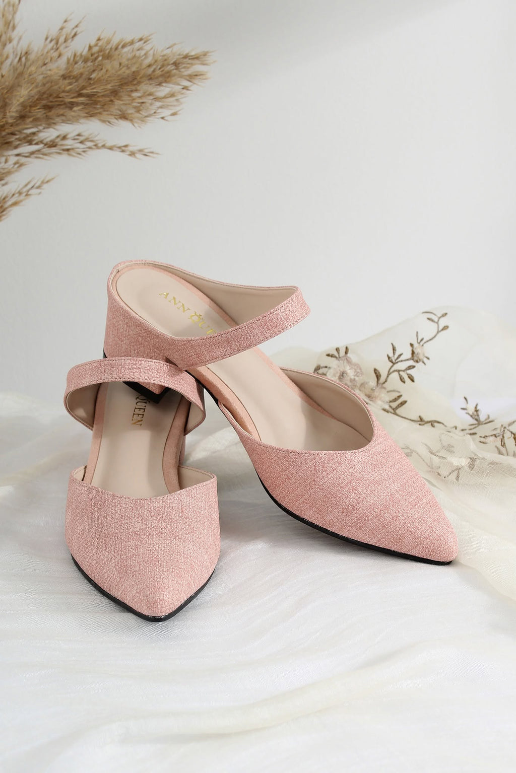 A pair of dusty pink pointed-toe slingback mule heels with a textured fabric upper and a low block heel