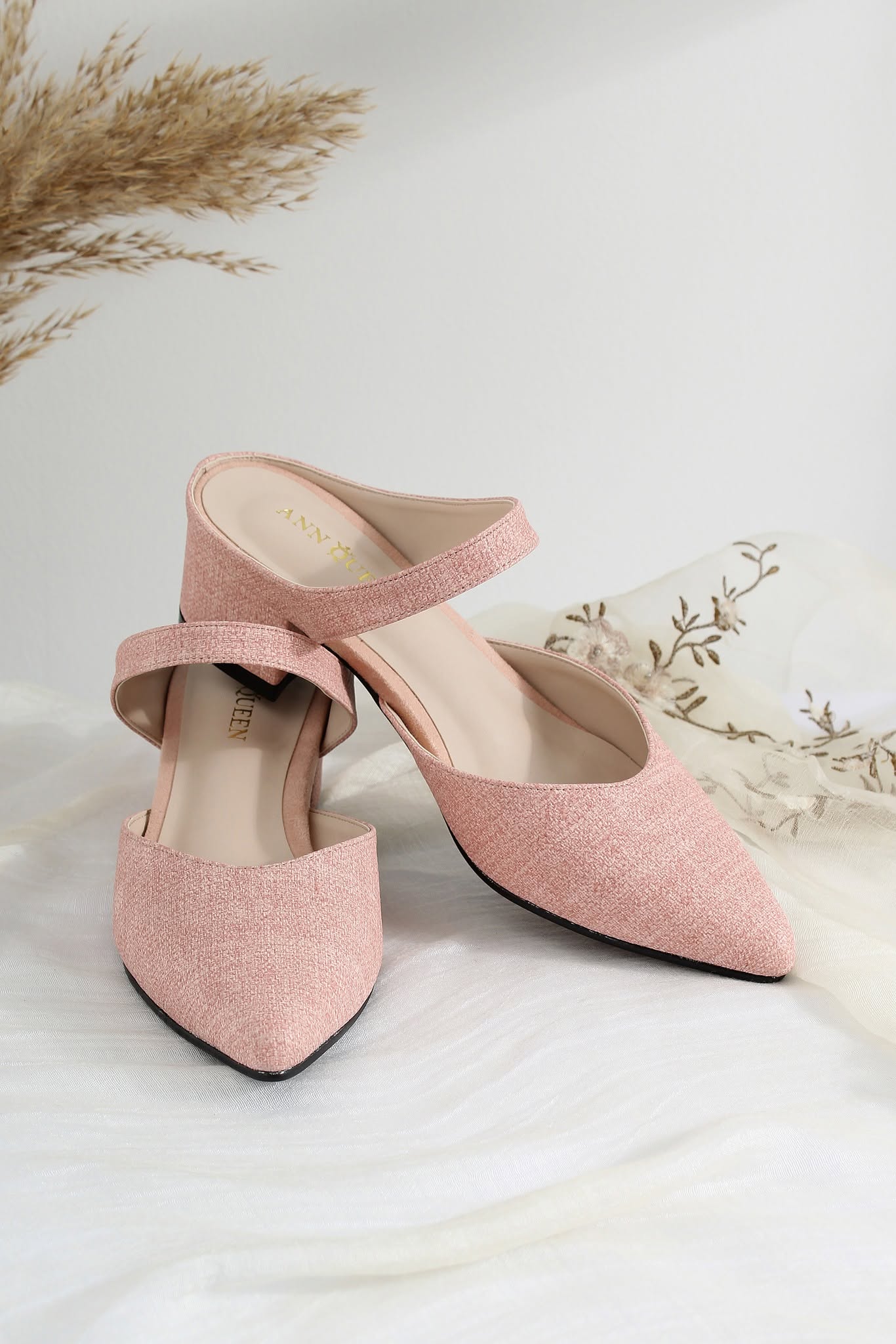 A pair of dusty pink pointed-toe slingback mule heels with a textured fabric upper and a low block heel