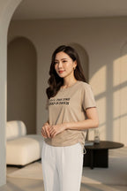 A woman wearing a beige graphic t-shirt with 'ALL THE TIME KEEP IN TOUCH' printed on the chest.