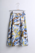 A high-waisted A-line skirt with a blue, white, and brown botanical leaf pattern on a mustard yellow background