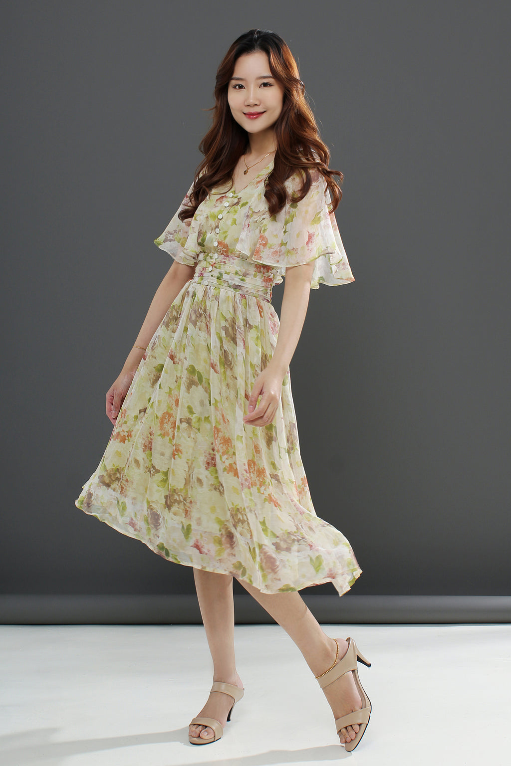 A woman wearing a floral midi dress with a gathered waist and a flowing skirt, in shades of pink and green