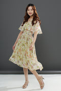 A woman wearing a floral midi dress with a gathered waist and a flowing skirt, in shades of pink and green