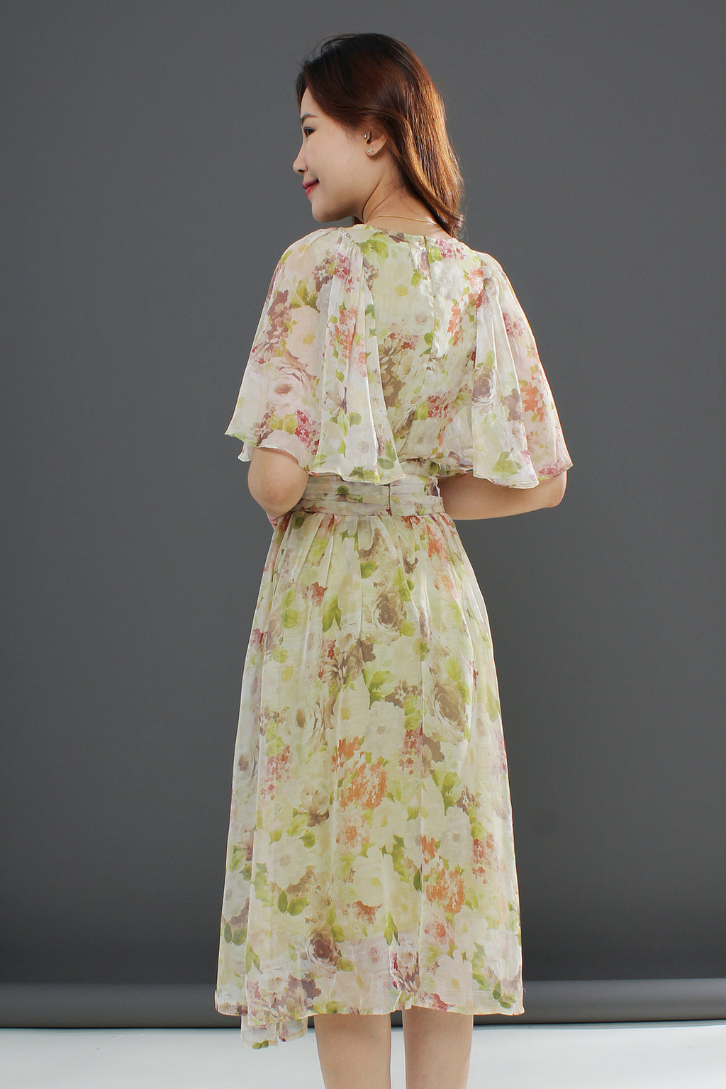 A woman wearing a floral midi dress with a gathered waist and a flowing skirt, in shades of green and pink