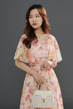 A woman wearing a floral midi dress with a gathered waist and a flowing skirt, in shades of pink and green