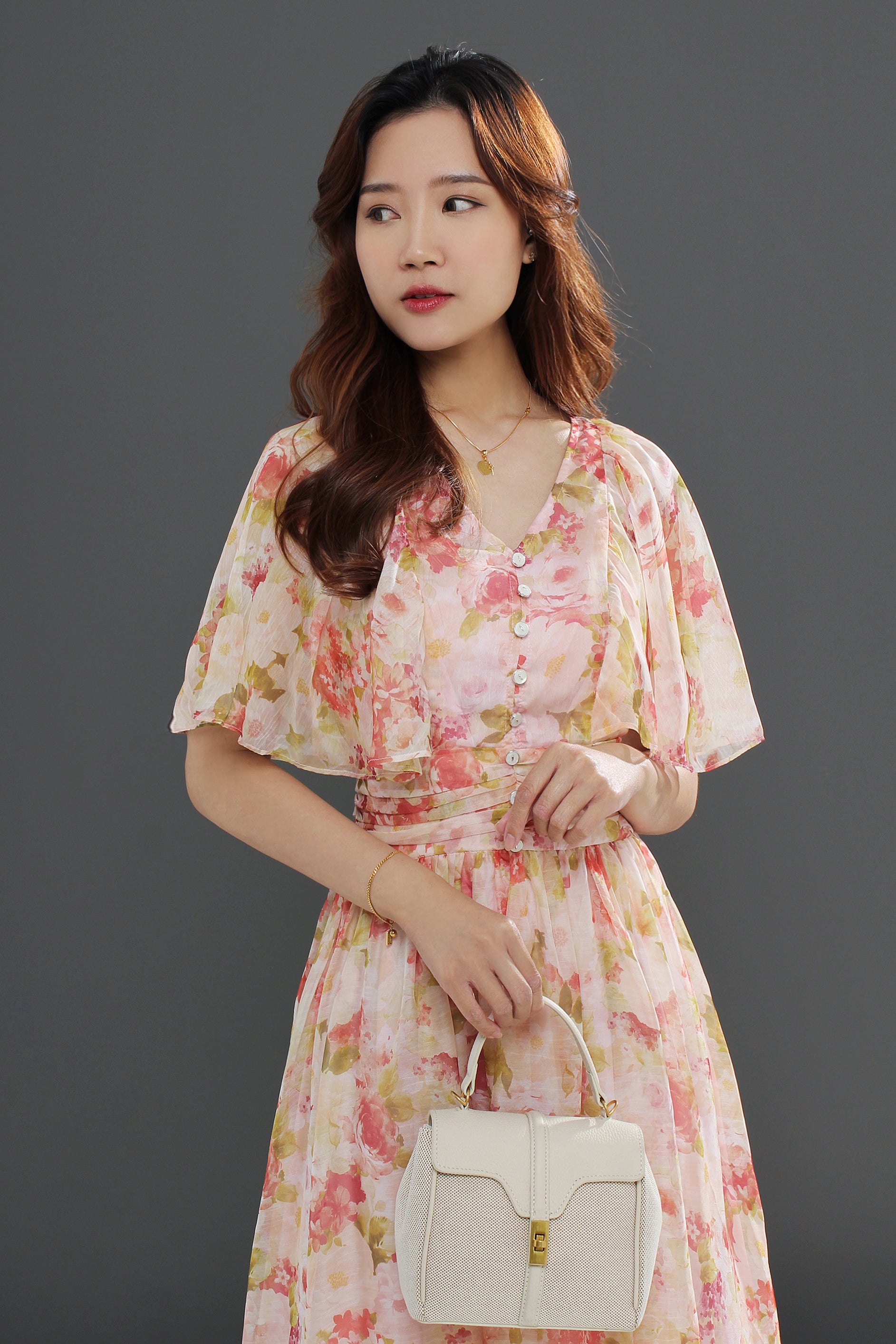 A woman wearing a floral midi dress with a gathered waist and a flowing skirt, in shades of pink and green
