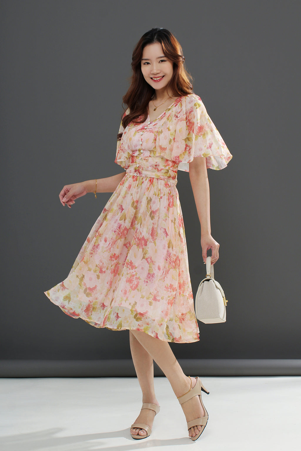 A woman wearing a floral midi dress with a gathered waist and a flowing skirt, in shades of pink and green
