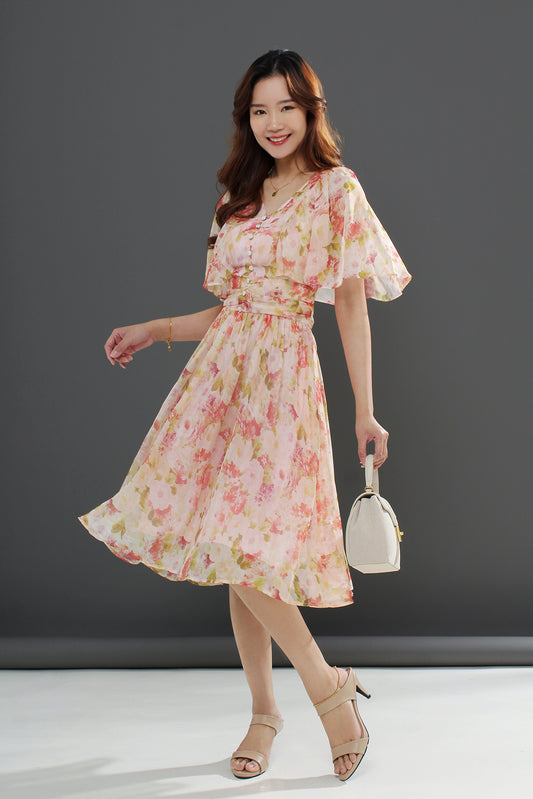 A woman wearing a floral midi dress with a gathered waist and a flowing skirt, in shades of pink and green