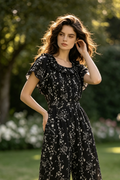 A woman  wearing a black short-sleeve jumpsuit with a white floral print.
