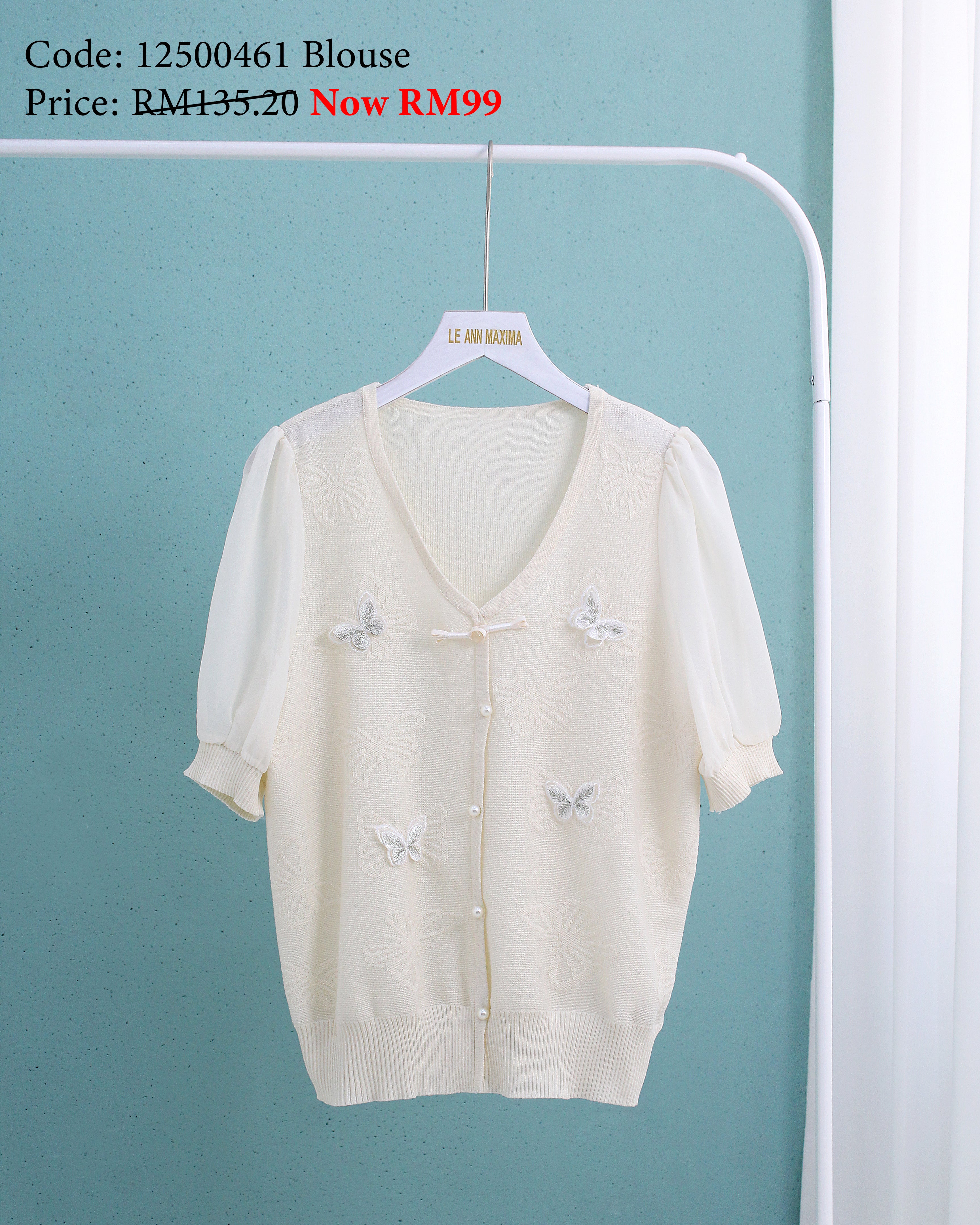 White blouse with butterfly designs on a hanger against a light blue wall.