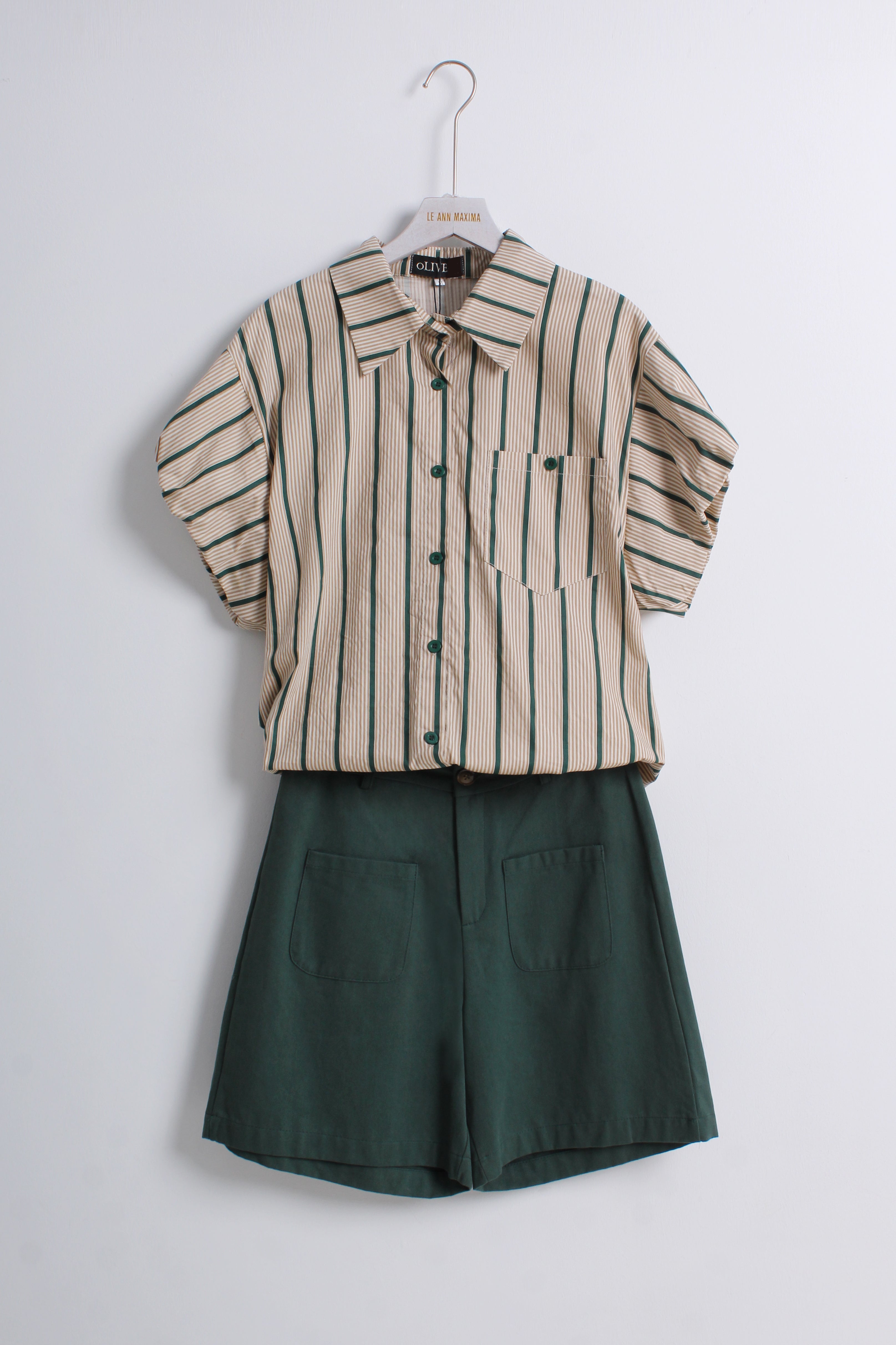 The set includes a short-sleeve button-front shirt in beige with dark green vertical stripes and a matching dark green pair of shorts with front patch pockets.
