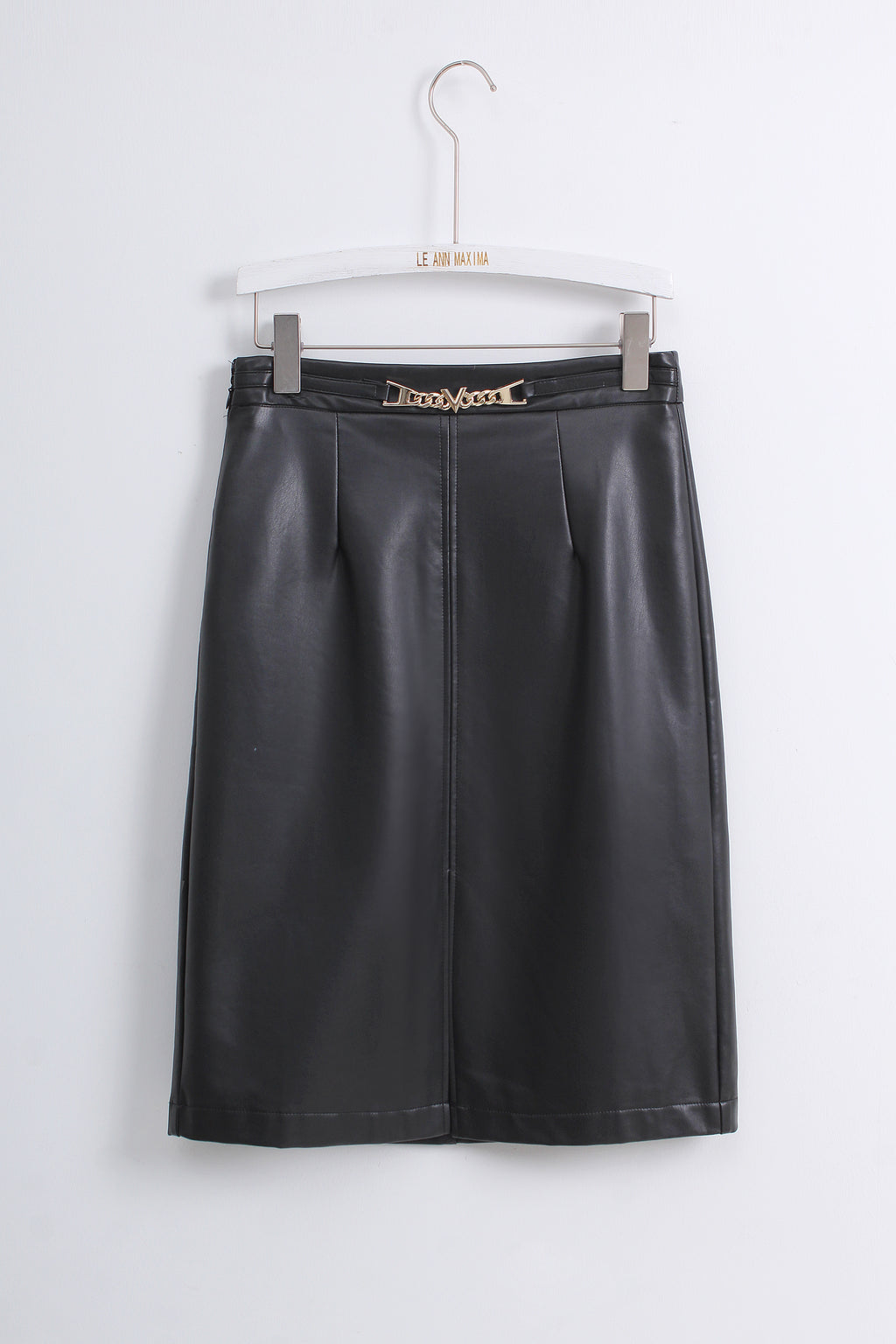 A black faux leather A-line skirt with pleated detailing and a gold-tone chain-link waistband, hanging on a white hanger against a light gray wall.