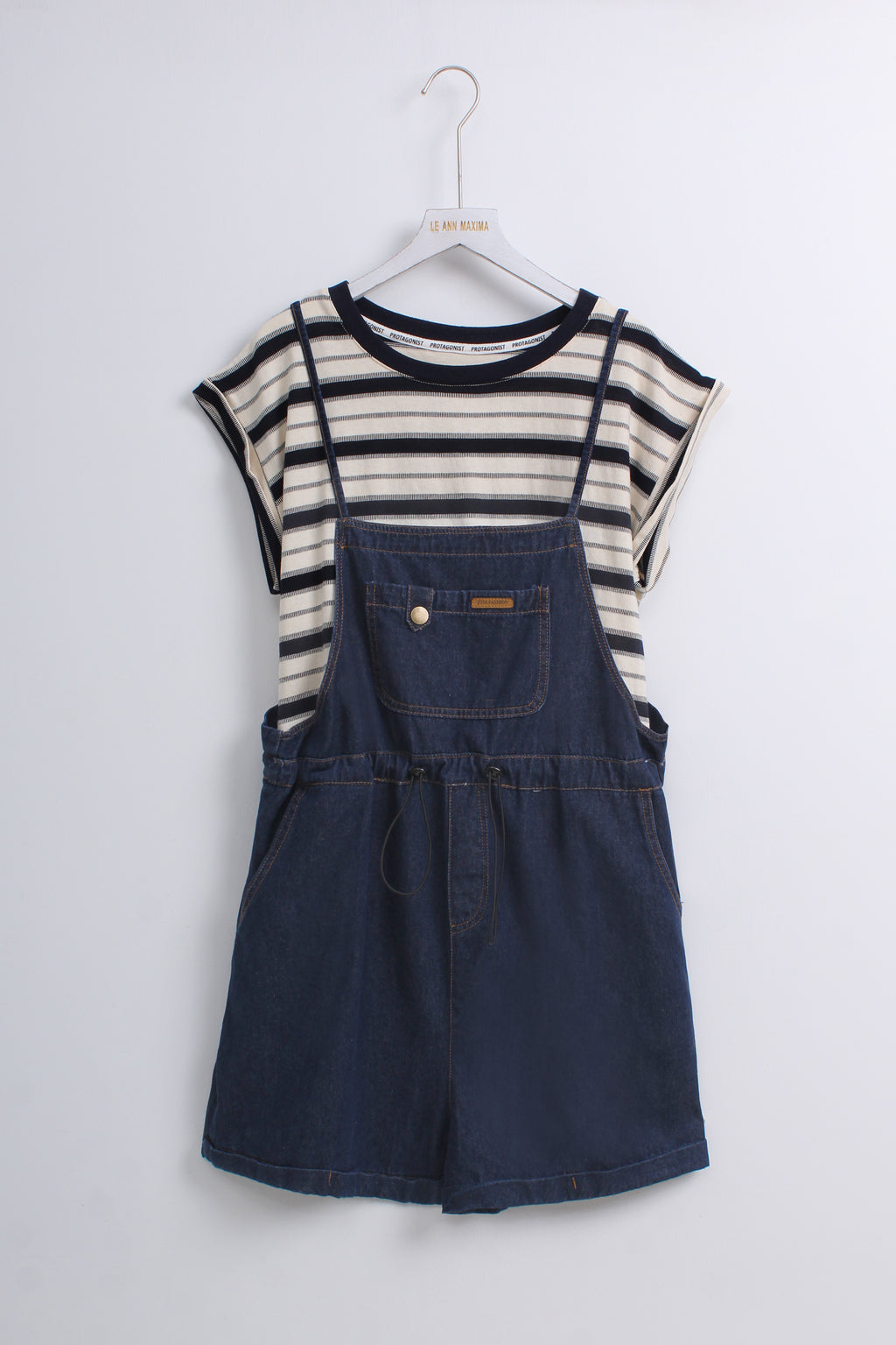 a navy blue denim overall romper layered over a cream and navy striped short-sleeve top.