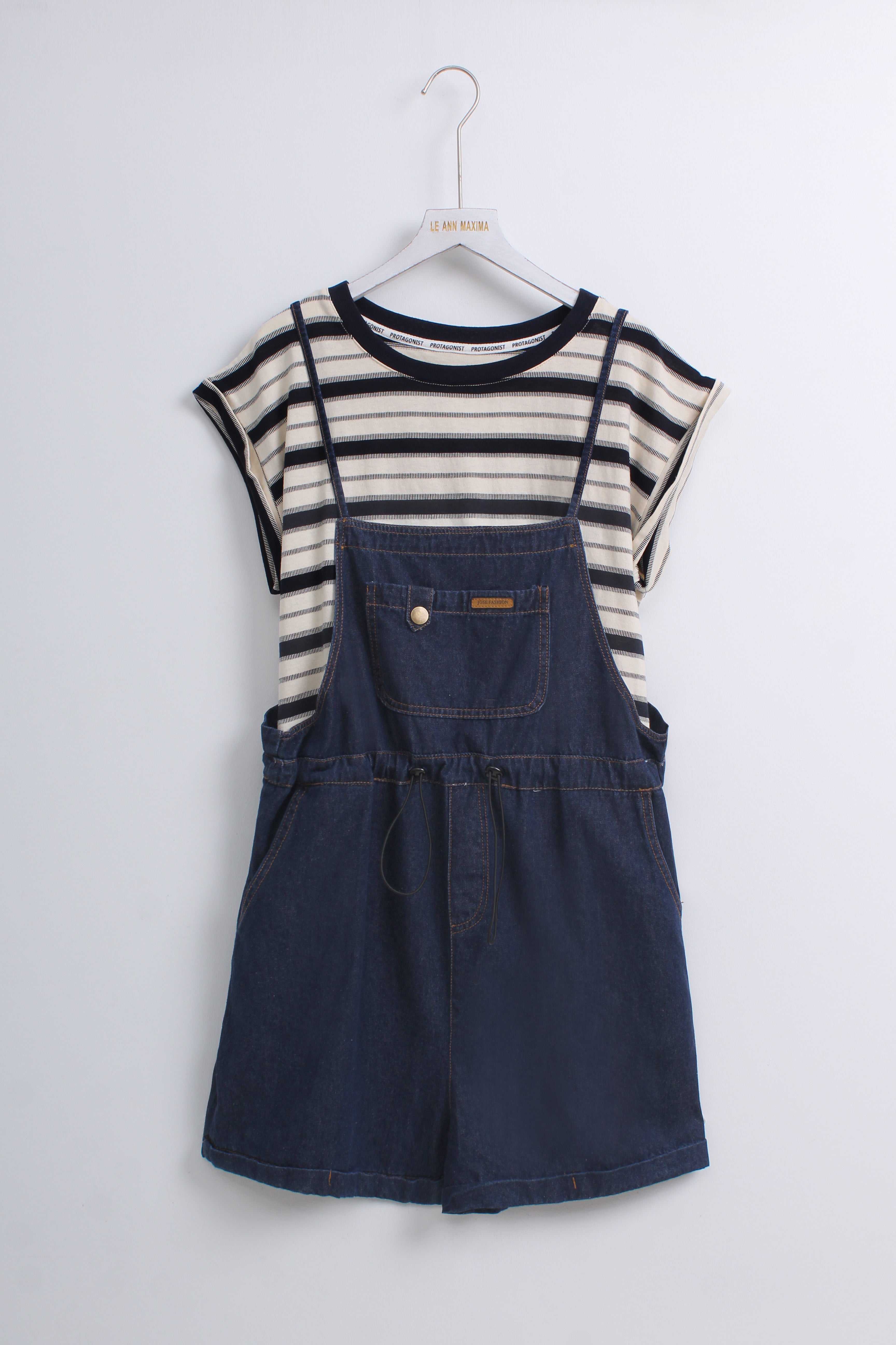 a navy blue denim overall romper layered over a cream and navy striped short-sleeve top.
