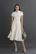 Woman wearing a white dress holding a green handbag against a gray background
