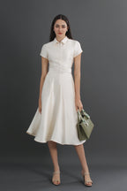 Woman wearing a white dress holding a green handbag against a gray background
