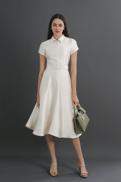 Woman wearing a white dress holding a green handbag against a gray background