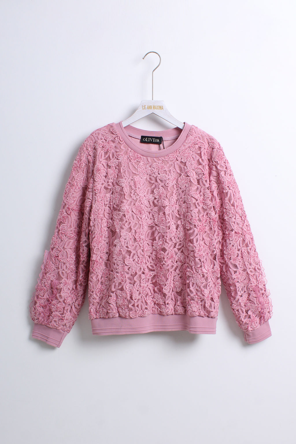 A pink textured lace knit crewneck sweater hanging on a white hanger against a plain light gray wall.
