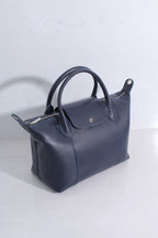 A dark navy blue leather handbag with double top handles and silver-tone hardware, photographed on a light gray surface against a matching light gray background.