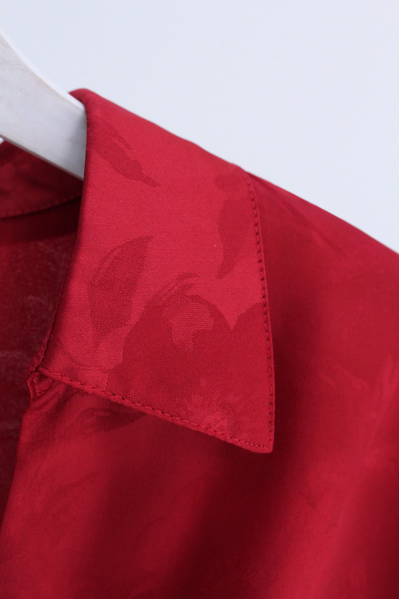 Close-up of a red collared shirt or blouse on a white hanger, showing the collar and upper chest area with a subtle tonal floral jacquard pattern.