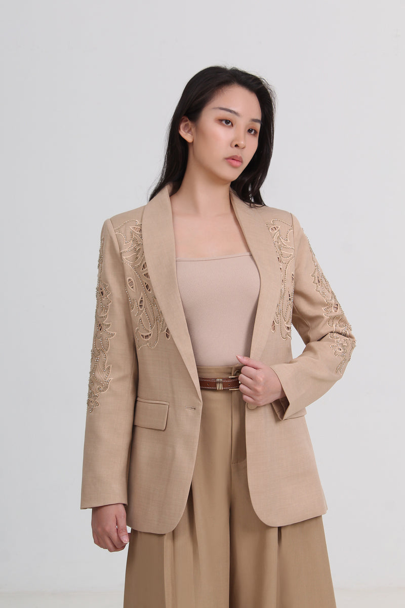 a beige tailored blazer with delicate floral embroidery on the lapels and shoulders, paired with a matching beige top and trousers by Le Ann Maxima