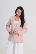 A woman wearing a light pink blazer with delicate floral embroidery on the sleeves, styled over a white top and white skirt