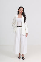 A woman modeling a white two-piece blazer and wide-leg pants set with a thin black belt, styled with a white top and black sandals by Le Ann Maxima