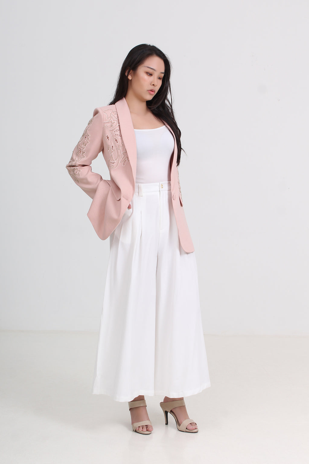 a light pink blazer with floral embroidery on the sleeves, worn over a white tank top and a long white pleated skirt, paired with beige high-heeled sandals by Le Ann Maxima