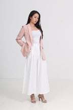a light pink blazer with floral embroidery on the sleeves, worn over a white tank top and a long white pleated skirt, paired with beige high-heeled sandals by Le Ann Maxima