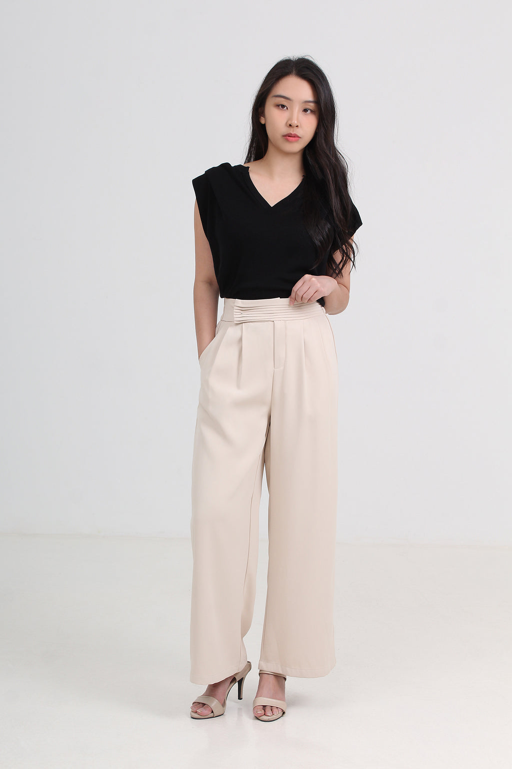 A woman modeling a black sleeveless V-neck top and high-waisted beige wide-leg trousers