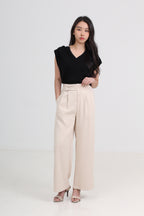 A woman modeling a black sleeveless V-neck top and high-waisted beige wide-leg trousers