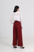 A woman is shown from the back wearing a white sheer long-sleeve blouse and high-waisted, wide-leg burgundy trousers with black heels