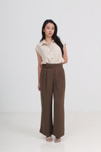 A woman wearing a cream sleeveless button-up shirt and high-waisted brown wide-leg trousers by Le Ann Maxima