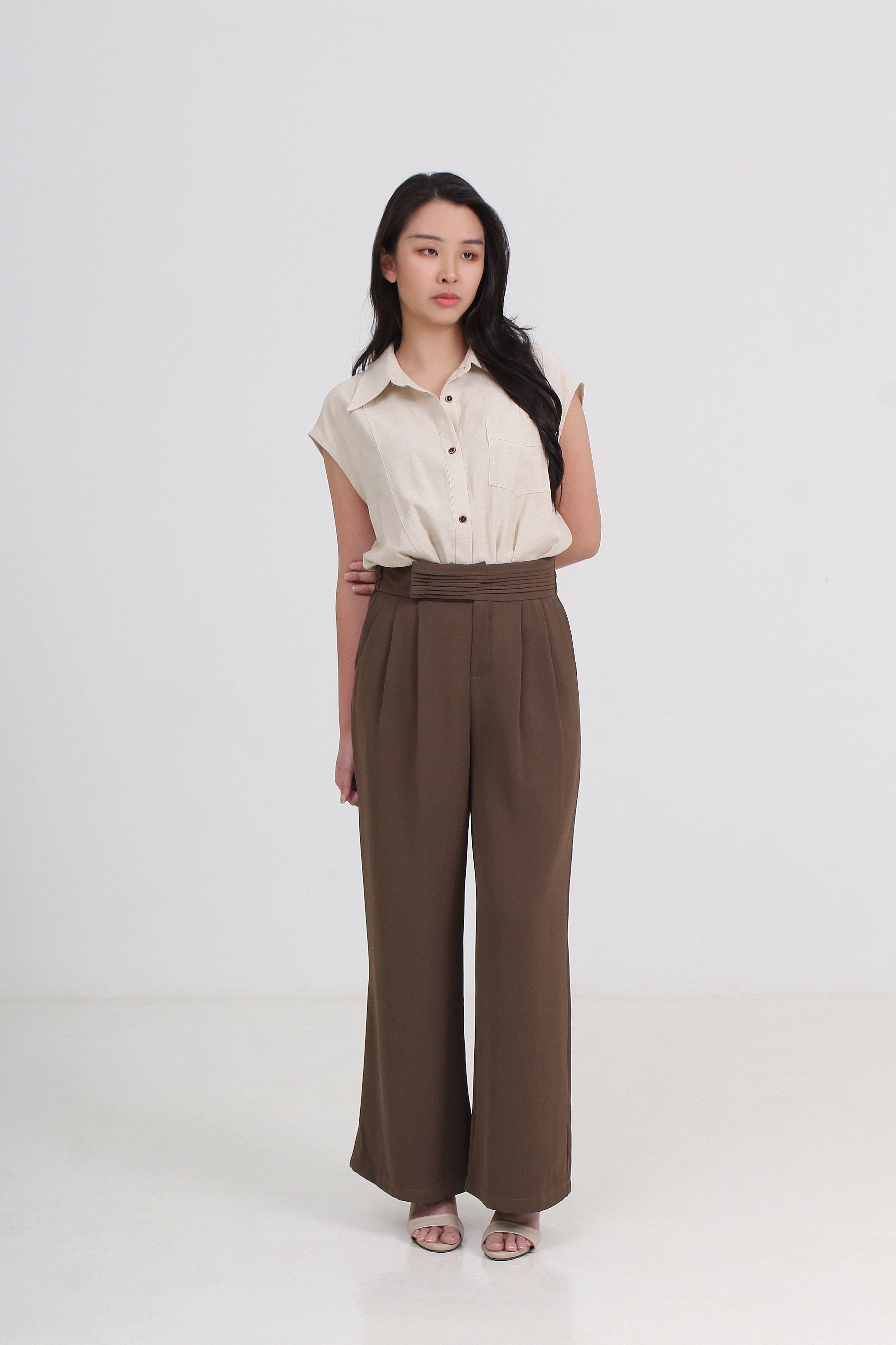 A woman wearing a cream sleeveless button-up shirt and high-waisted brown wide-leg trousers by Le Ann Maxima