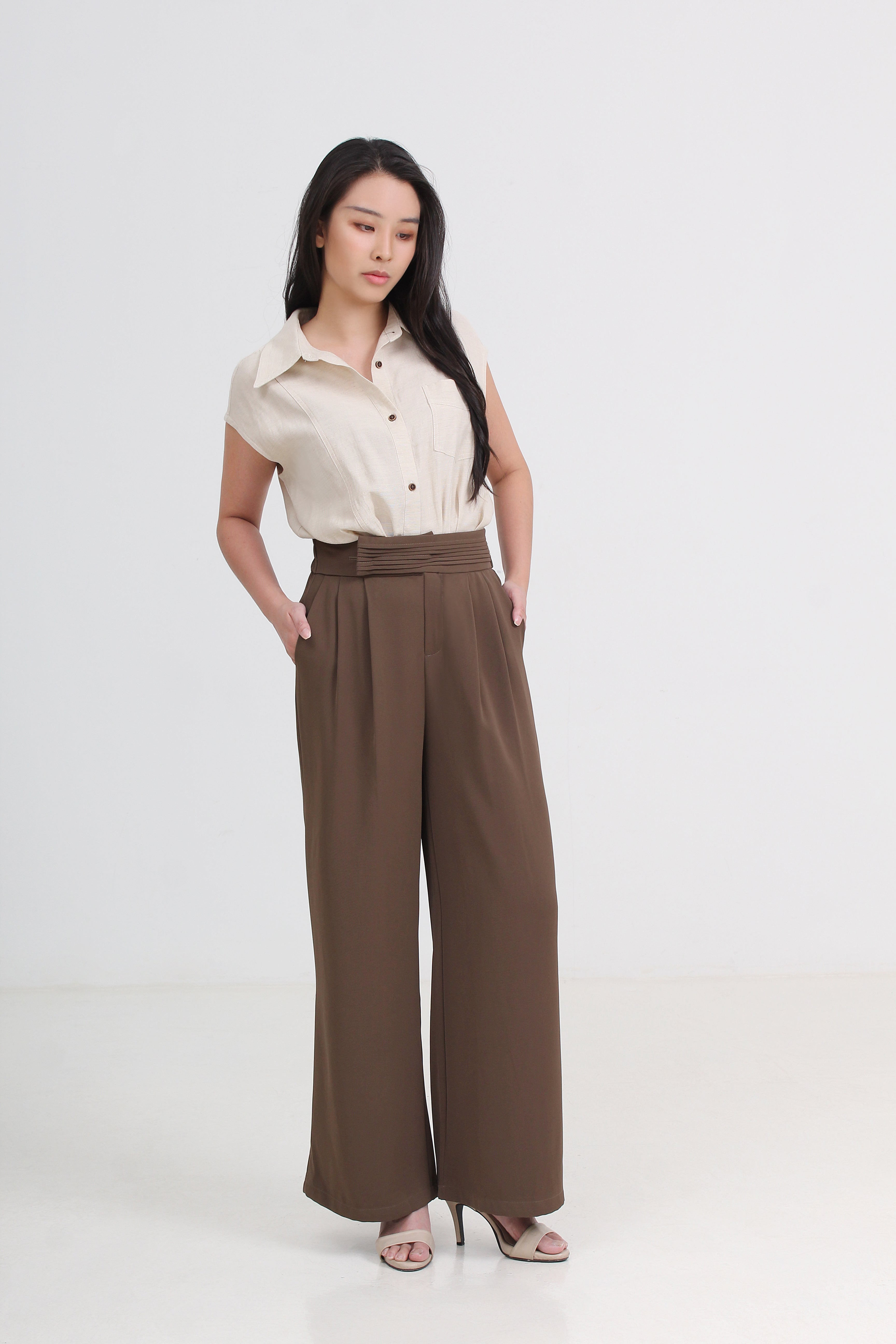 A woman modeling a beige short-sleeve button-up shirt and brown wide-leg trousers