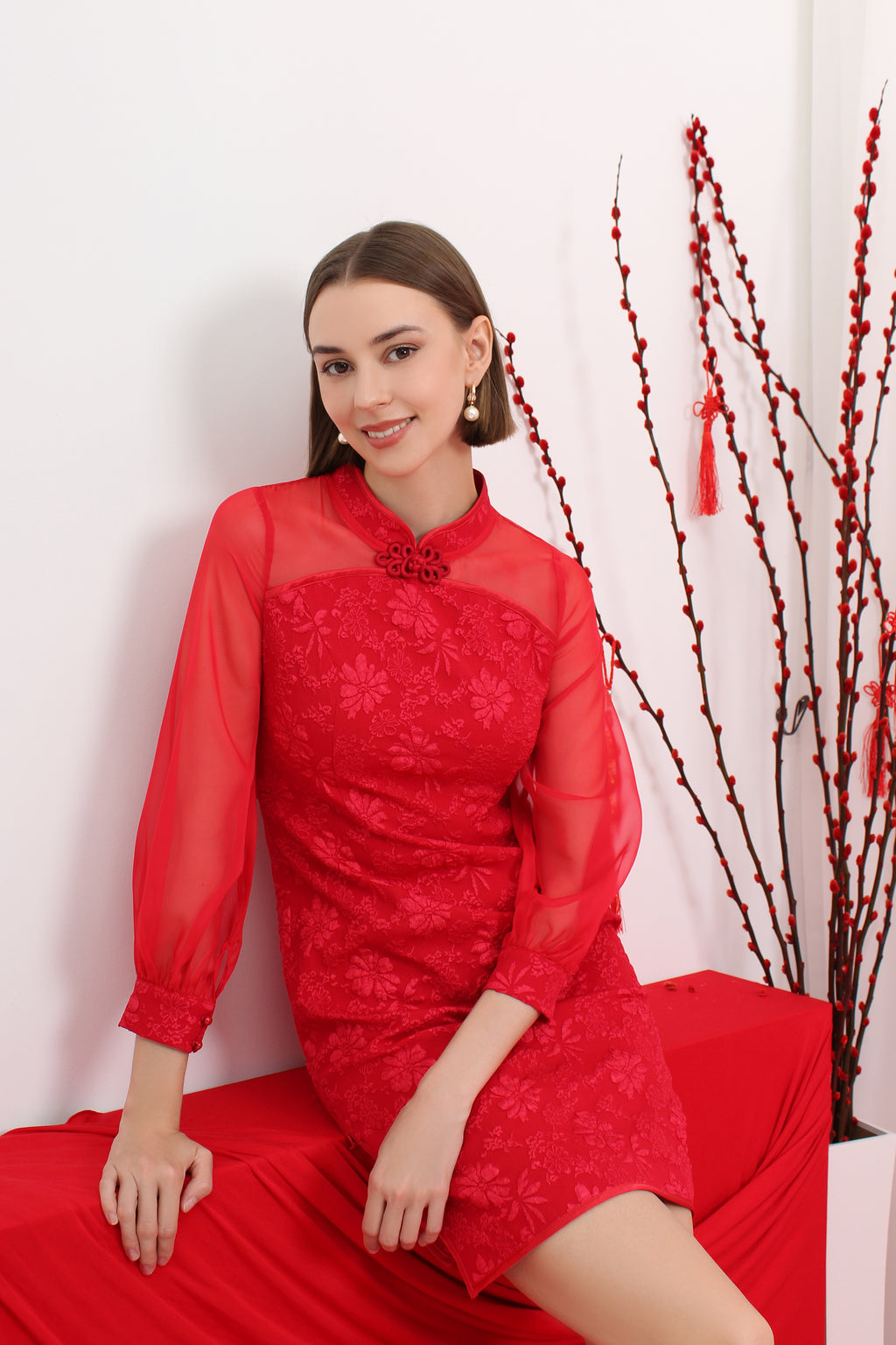 Woman in a red cheongsam dress sitting on a red couch with a white background and decorative elements.