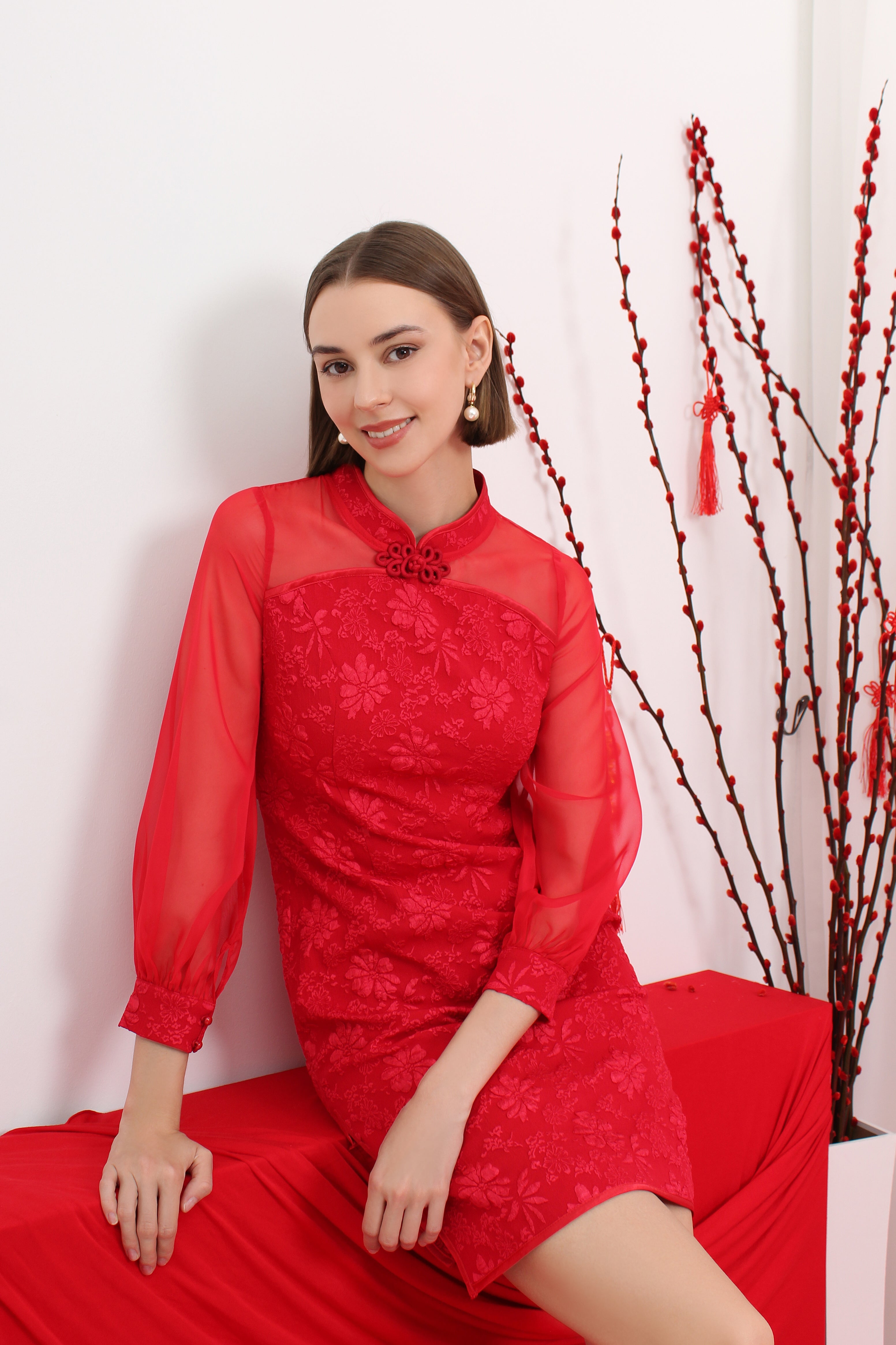 Woman in a red cheongsam dress sitting on a red couch with a white background and decorative elements.