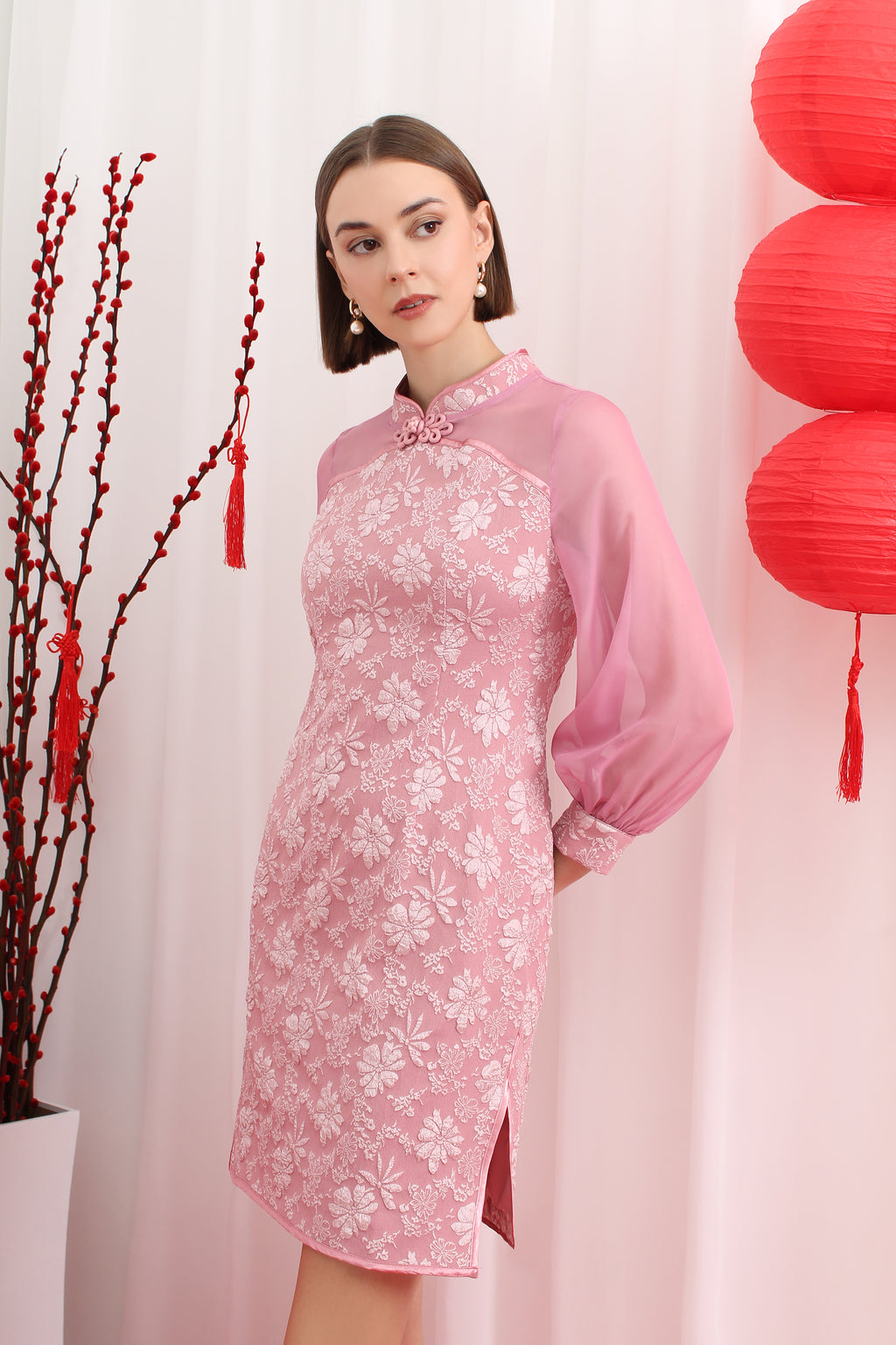 Woman wearing a pink floral cheongsam dress with red lanterns and branches in the background