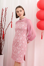 Woman wearing a pink floral cheongsam dress with red lanterns and branches in the background