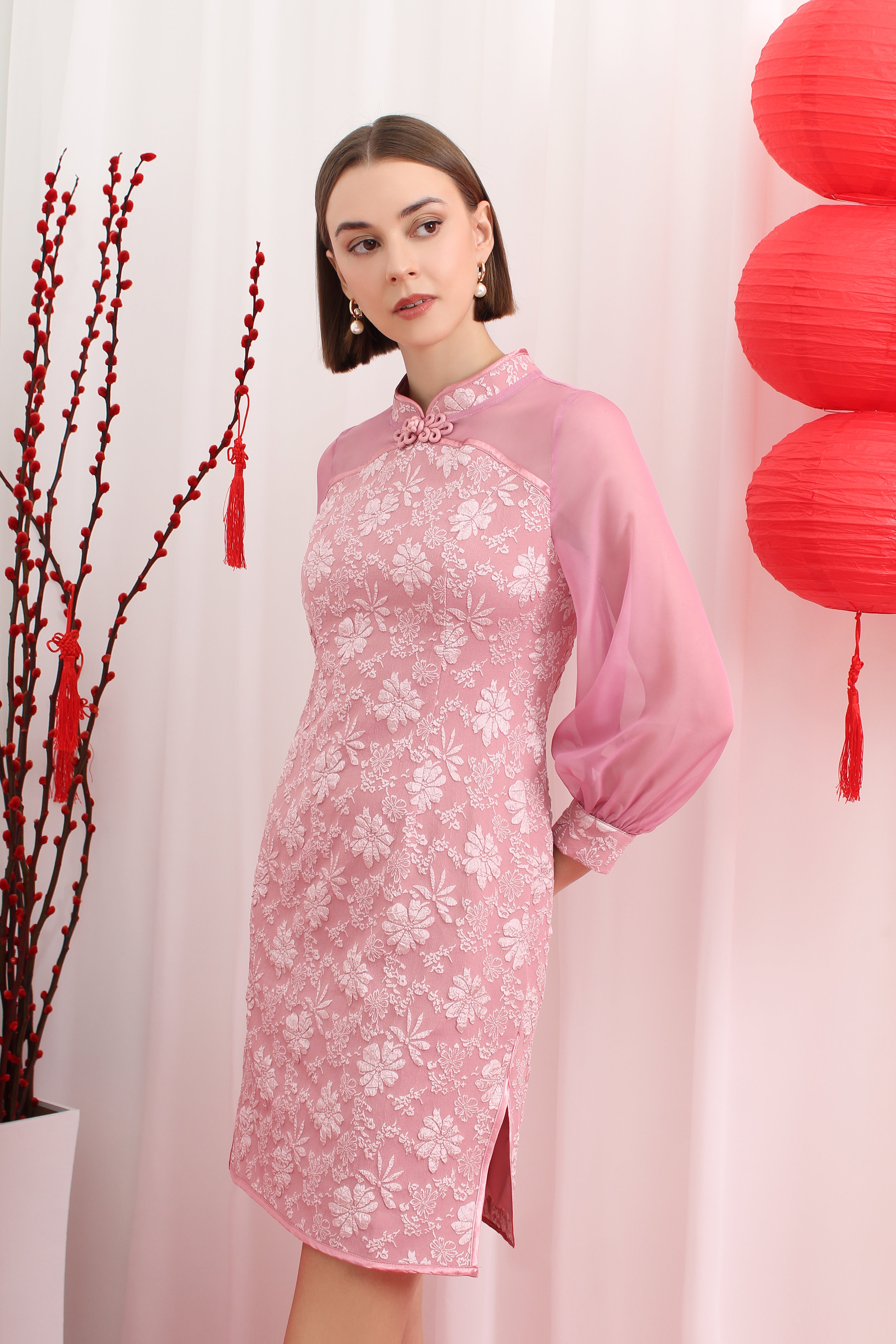 Woman wearing a pink floral cheongsam dress with red lanterns and branches in the background
