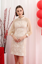 Woman wearing a sheer long sleeve mandarin collar champagne cheongsam dress against a white background with red lanterns and branches