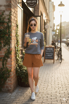 Woman walking on a sidewalk holding a coffee cup, wearing sunglasses and a casual outfit with snoopy and friends graphics