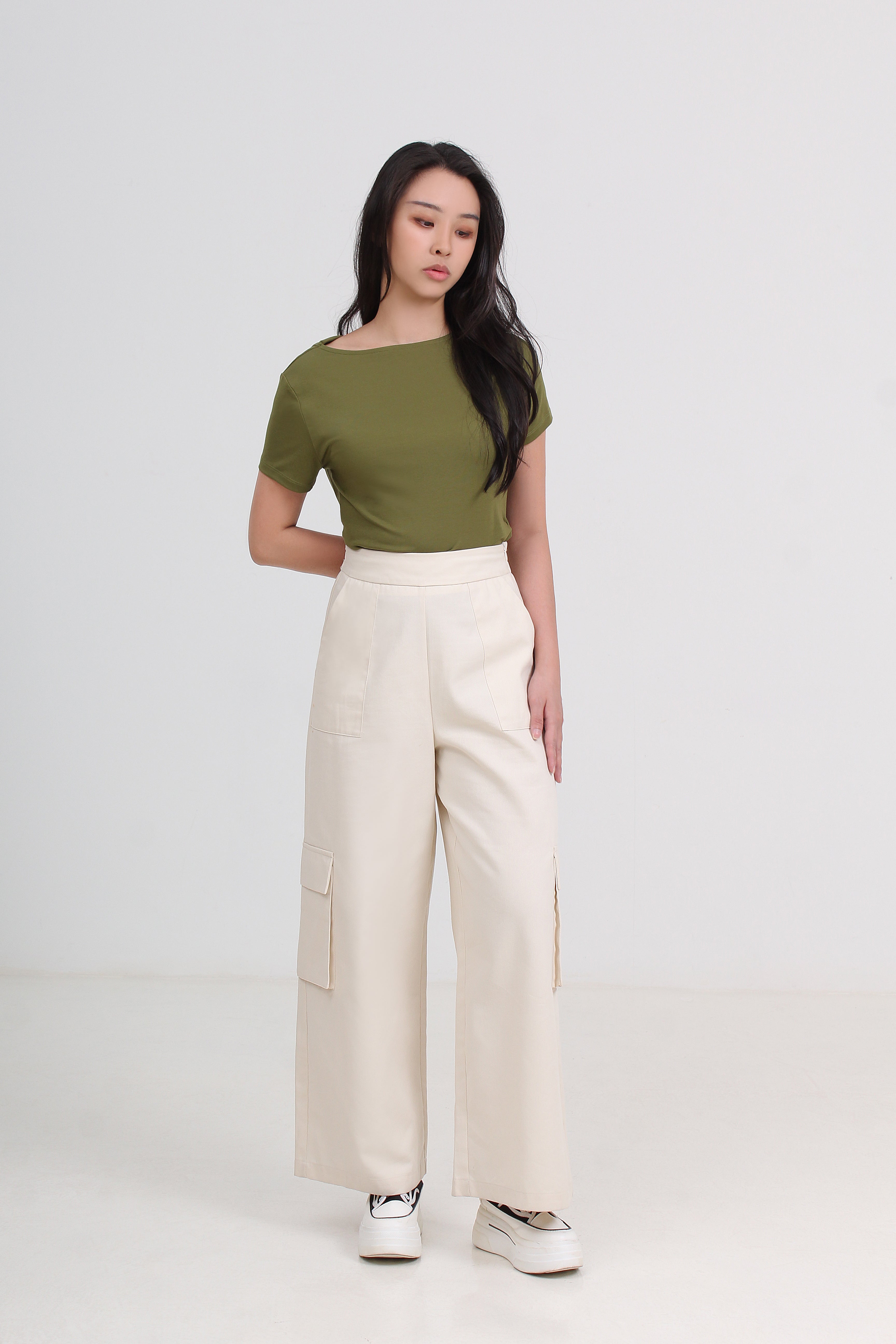 A woman modeling a short-sleeve olive green top and high-waisted cream wide-leg cargo pants.