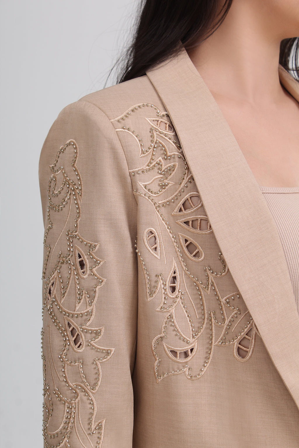 Close-up of a beige tailored jacket with intricate floral eyelet embroidery and bead detailing on the sleeve and shoulder by Le Ann Maxima