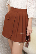 Le Ann Maxima rust brown mini skirt featuring a layered front panel, pleated detail, and decorative flap pocket.